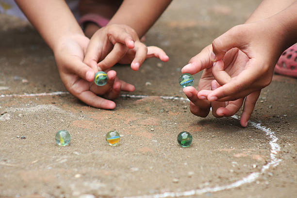Children playing marbles in a chalk circle on a dusty street—Kancha street game